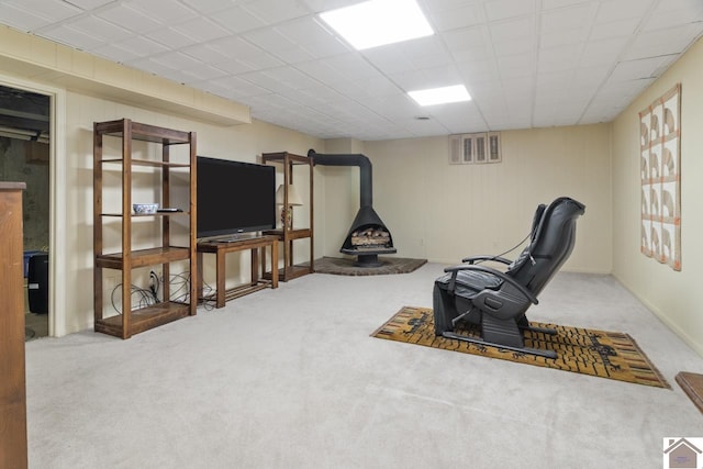 living area with light carpet, a wood stove, and a paneled ceiling