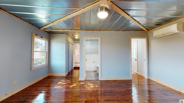 unfurnished bedroom featuring connected bathroom, dark wood-type flooring, and an AC wall unit