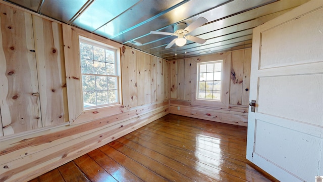 empty room with wooden walls, ceiling fan, and hardwood / wood-style flooring