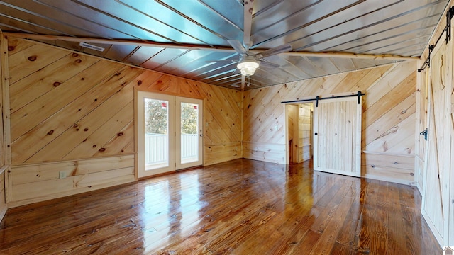 additional living space with ceiling fan, dark wood-type flooring, a barn door, vaulted ceiling, and wooden walls