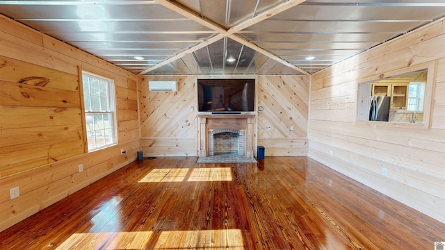 unfurnished living room featuring dark hardwood / wood-style flooring, wood walls, a brick fireplace, and a wall mounted air conditioner