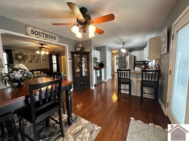 dining area with plenty of natural light, a textured ceiling, dark wood-type flooring, and ceiling fan with notable chandelier