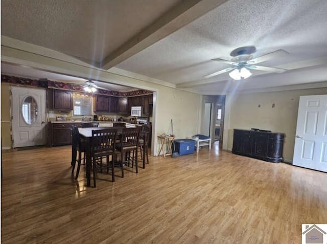 dining room with hardwood / wood-style floors, ceiling fan, a textured ceiling, and beam ceiling