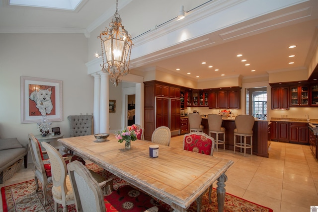 tiled dining area with a chandelier, ornamental molding, decorative columns, and vaulted ceiling with skylight