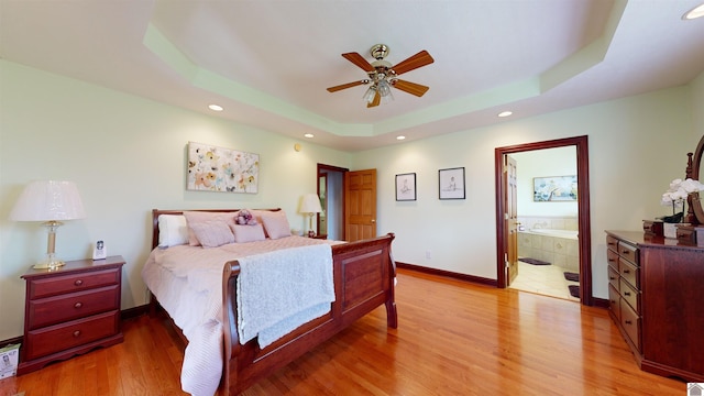 bedroom with a tray ceiling, ensuite bath, ceiling fan, and light wood-type flooring