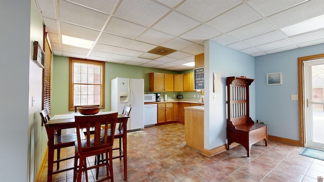 kitchen featuring light tile floors, a drop ceiling, and white appliances