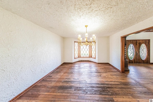 empty room featuring dark wood-type flooring, a chandelier, and a textured ceiling