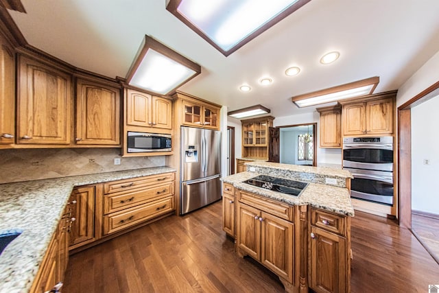 kitchen featuring a kitchen island, light stone countertops, tasteful backsplash, dark wood-type flooring, and appliances with stainless steel finishes