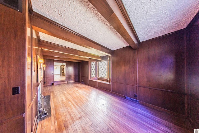 spare room with wood walls, a textured ceiling, wood-type flooring, and beamed ceiling