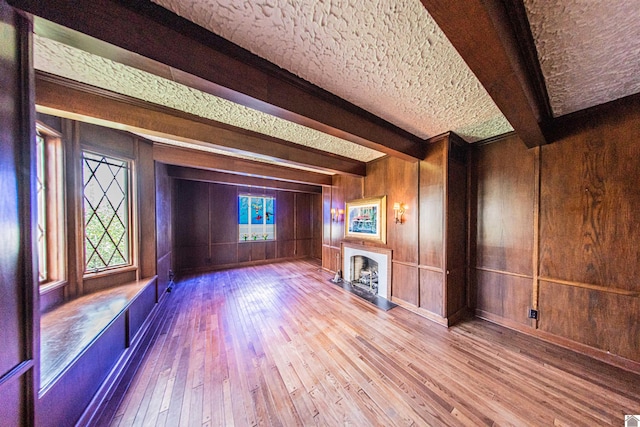 interior space with hardwood / wood-style flooring, wood walls, a textured ceiling, and beam ceiling