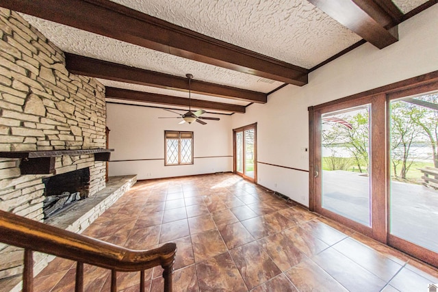 unfurnished living room with a stone fireplace, beam ceiling, a textured ceiling, and a wealth of natural light