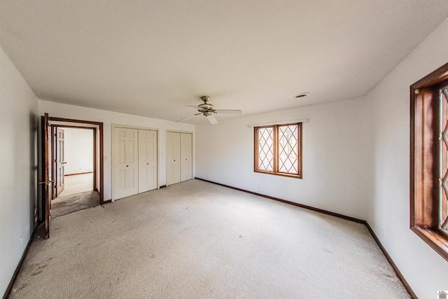 unfurnished bedroom with multiple closets, ceiling fan, and light carpet