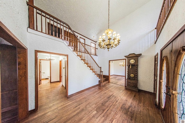 interior space with a notable chandelier, a textured ceiling, high vaulted ceiling, and hardwood / wood-style floors