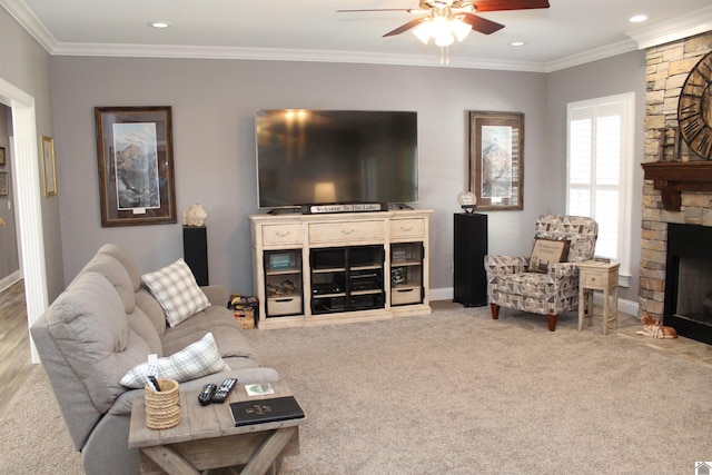 living room with a stone fireplace, crown molding, ceiling fan, and light colored carpet