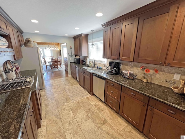 kitchen featuring appliances with stainless steel finishes, dark stone countertops, backsplash, hanging light fixtures, and light tile flooring