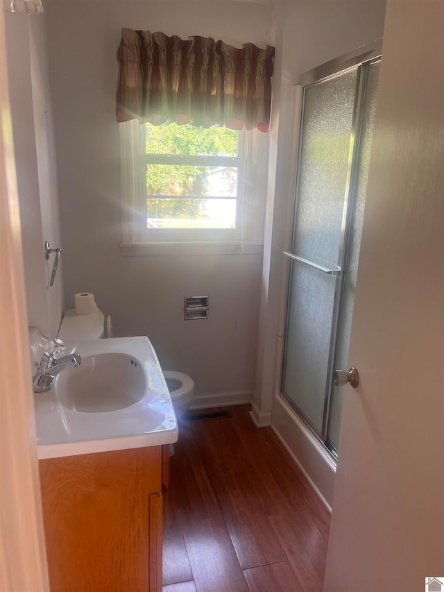 bathroom with hardwood / wood-style floors, a shower with door, vanity, and toilet