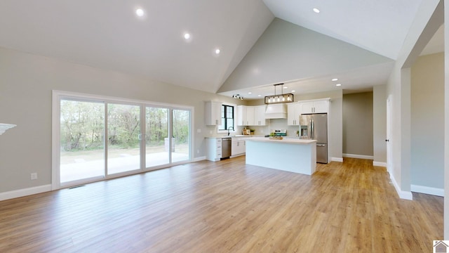 kitchen with high vaulted ceiling, decorative light fixtures, stainless steel appliances, white cabinets, and light wood-type flooring