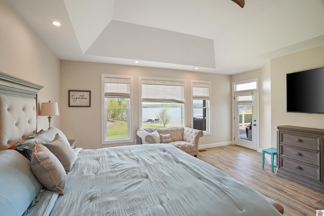 bedroom featuring light hardwood / wood-style flooring, a tray ceiling, and access to outside