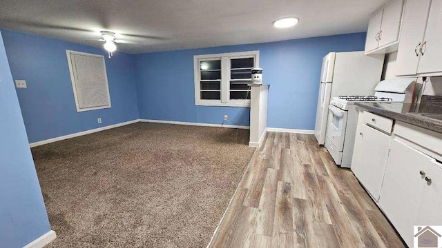kitchen featuring white cabinets, dark countertops, baseboards, and white gas range