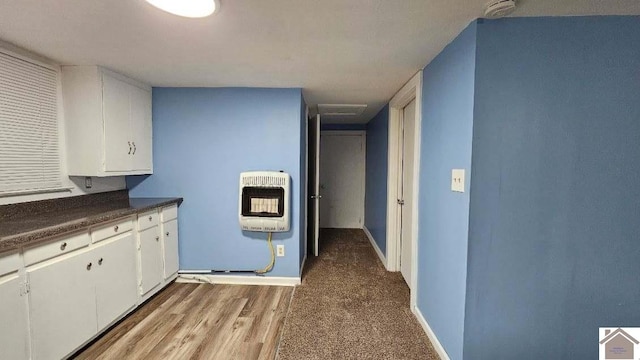 kitchen with white cabinets, dark countertops, baseboards, heating unit, and wood finished floors