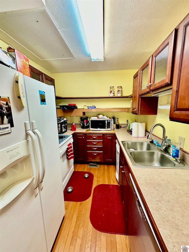 kitchen with light wood-type flooring, a textured ceiling, white appliances, and sink