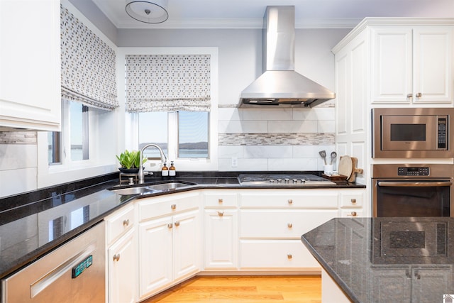 kitchen featuring wall chimney range hood, appliances with stainless steel finishes, white cabinets, dark stone counters, and sink