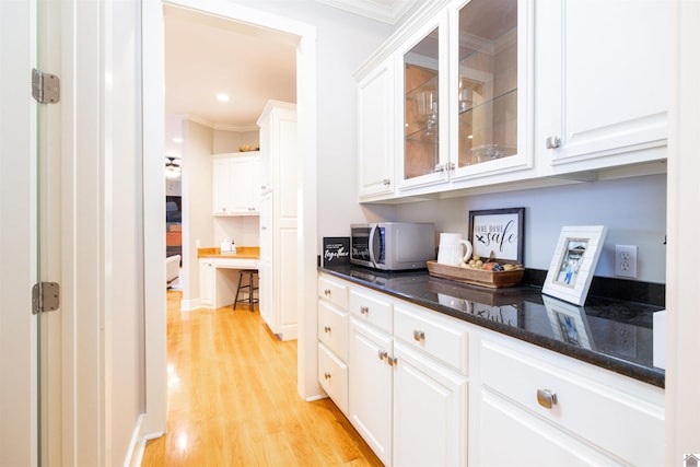 kitchen with dark stone counters, ornamental molding, white cabinets, and light wood-type flooring