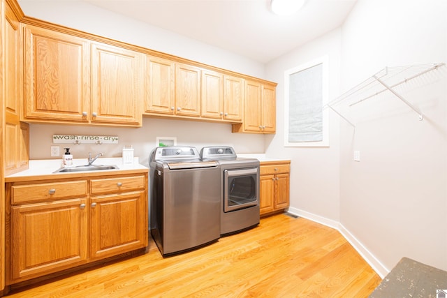 laundry area featuring separate washer and dryer, sink, light hardwood / wood-style flooring, and cabinets