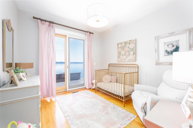 bedroom with access to outside, light wood-type flooring, and a water view