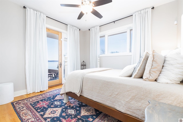 bedroom featuring access to outside, hardwood / wood-style flooring, ceiling fan, and a water view