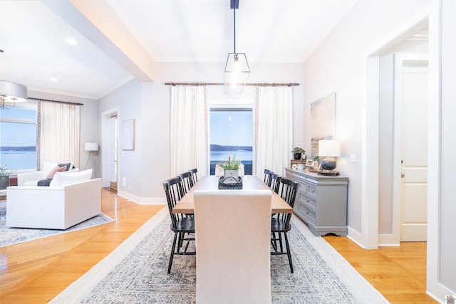 dining room featuring ornamental molding, light wood-type flooring, and a water view