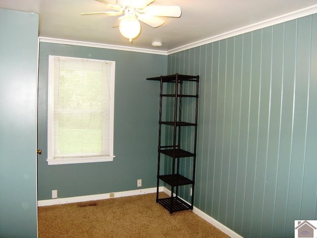 carpeted empty room with ceiling fan, crown molding, and wood walls