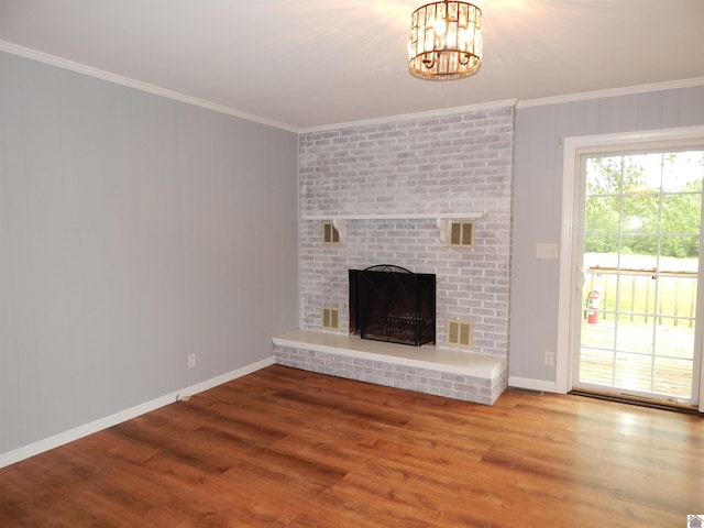 unfurnished living room featuring brick wall, a brick fireplace, an inviting chandelier, crown molding, and hardwood / wood-style floors