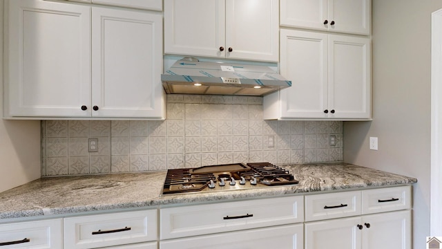 kitchen with white cabinets, backsplash, light stone countertops, and stainless steel gas cooktop