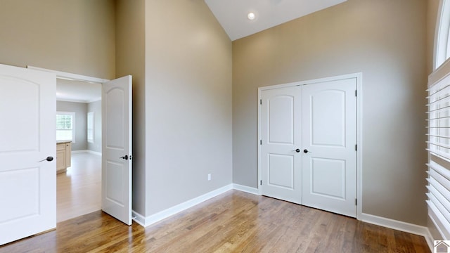 unfurnished bedroom with high vaulted ceiling, a closet, and light hardwood / wood-style floors