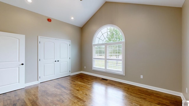 spare room featuring high vaulted ceiling, a healthy amount of sunlight, and wood-type flooring