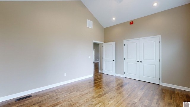 unfurnished bedroom with high vaulted ceiling, a closet, and wood-type flooring