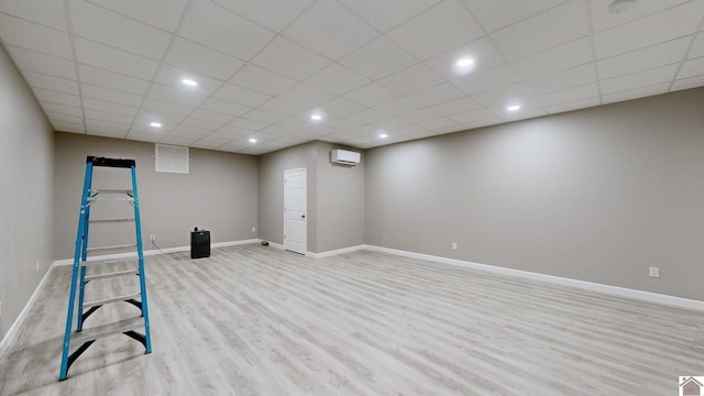 interior space featuring a drop ceiling, a wall mounted AC, and light hardwood / wood-style flooring