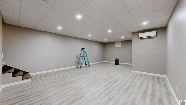 basement featuring light hardwood / wood-style flooring, a wall mounted AC, and a drop ceiling