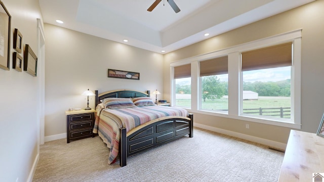 bedroom with light carpet, a raised ceiling, and ceiling fan