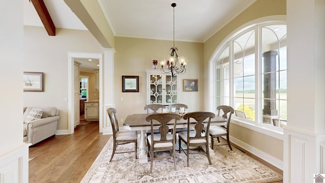 dining space featuring decorative columns, crown molding, light hardwood / wood-style flooring, a notable chandelier, and beamed ceiling