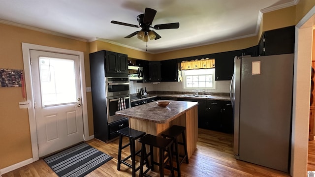 kitchen with appliances with stainless steel finishes, tasteful backsplash, a center island, light hardwood / wood-style floors, and crown molding