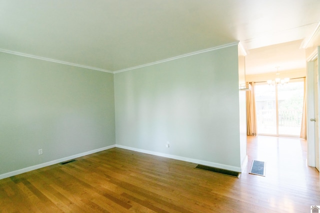 spare room featuring hardwood / wood-style flooring, ornamental molding, and a chandelier