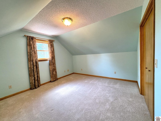 bonus room with vaulted ceiling, light colored carpet, and a textured ceiling