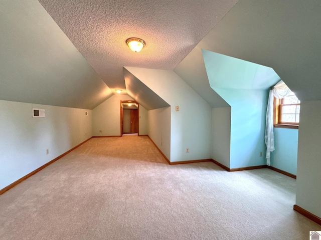 additional living space featuring vaulted ceiling, light colored carpet, and a textured ceiling