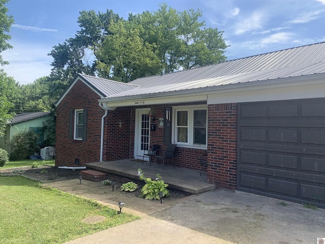 ranch-style house featuring driveway, metal roof, an attached garage, a porch, and brick siding