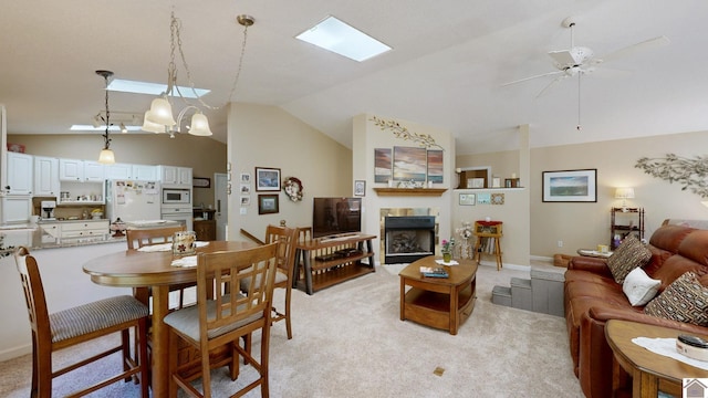 living room with vaulted ceiling with skylight, ceiling fan, light colored carpet, and a fireplace