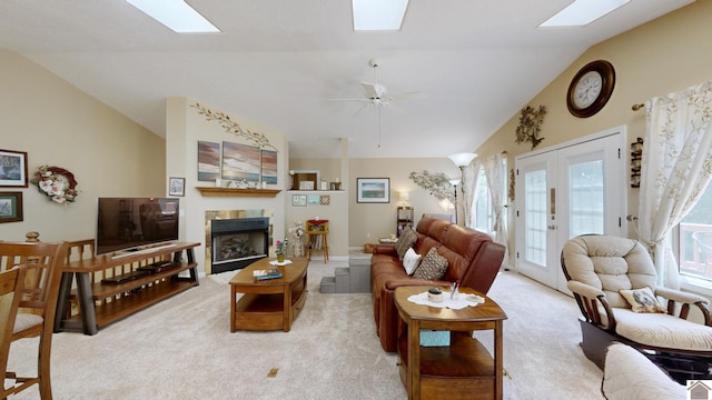 living room featuring light carpet, french doors, lofted ceiling with skylight, ceiling fan, and a fireplace