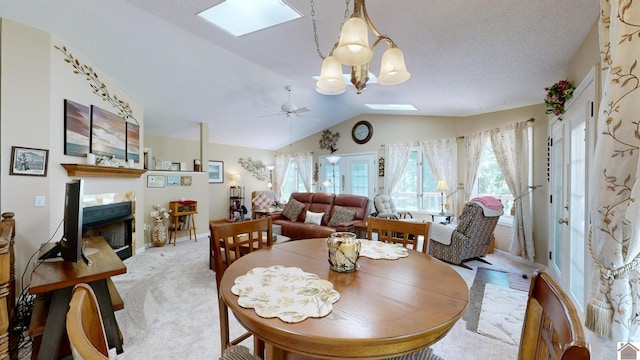 dining room with lofted ceiling with skylight, a fireplace, light colored carpet, and ceiling fan with notable chandelier