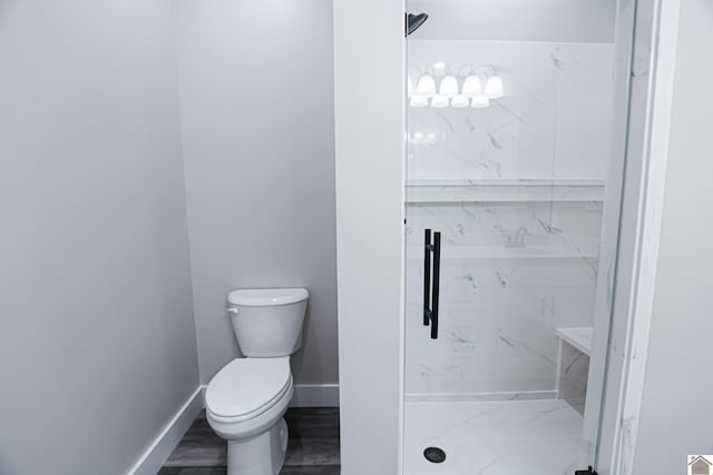 bathroom featuring baseboards, wood finished floors, toilet, and a marble finish shower